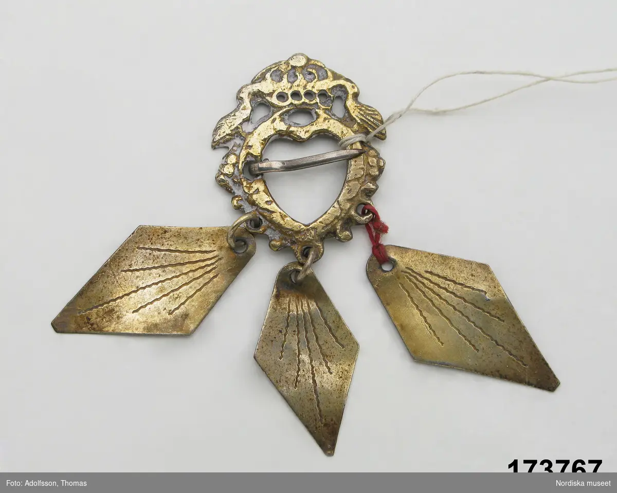 Liten sölja av förgyllt silver med krona och 2 fåglar samt 3 rombiska hängen.

Berit Eldvik 2004