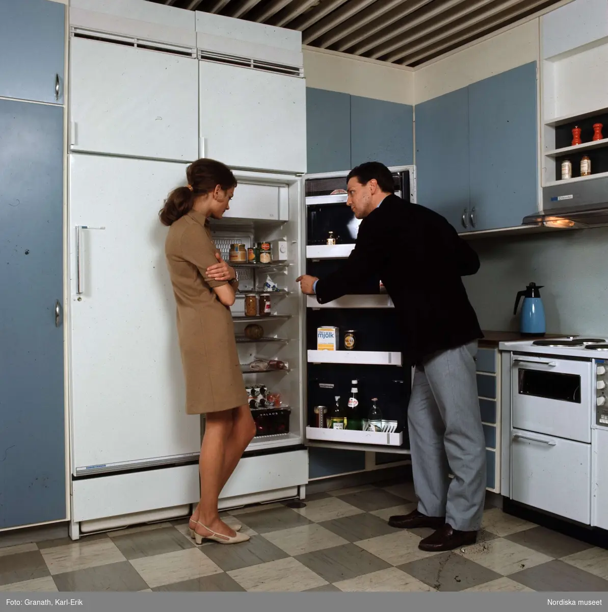 Man och kvinna framför kylskåp i gråblått kök.