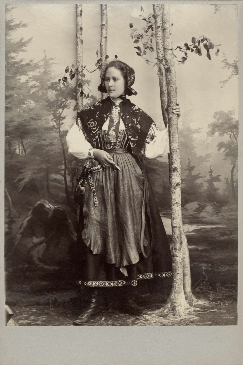 En kvinna poserar i en folkdräkt med skinnförkläde
