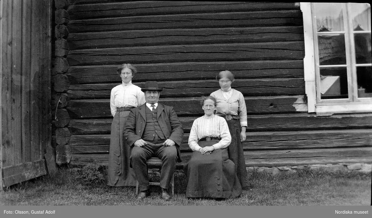 Gruppfoto av tre kvinnor och en man framför husvägg, från början av 1900-talet.