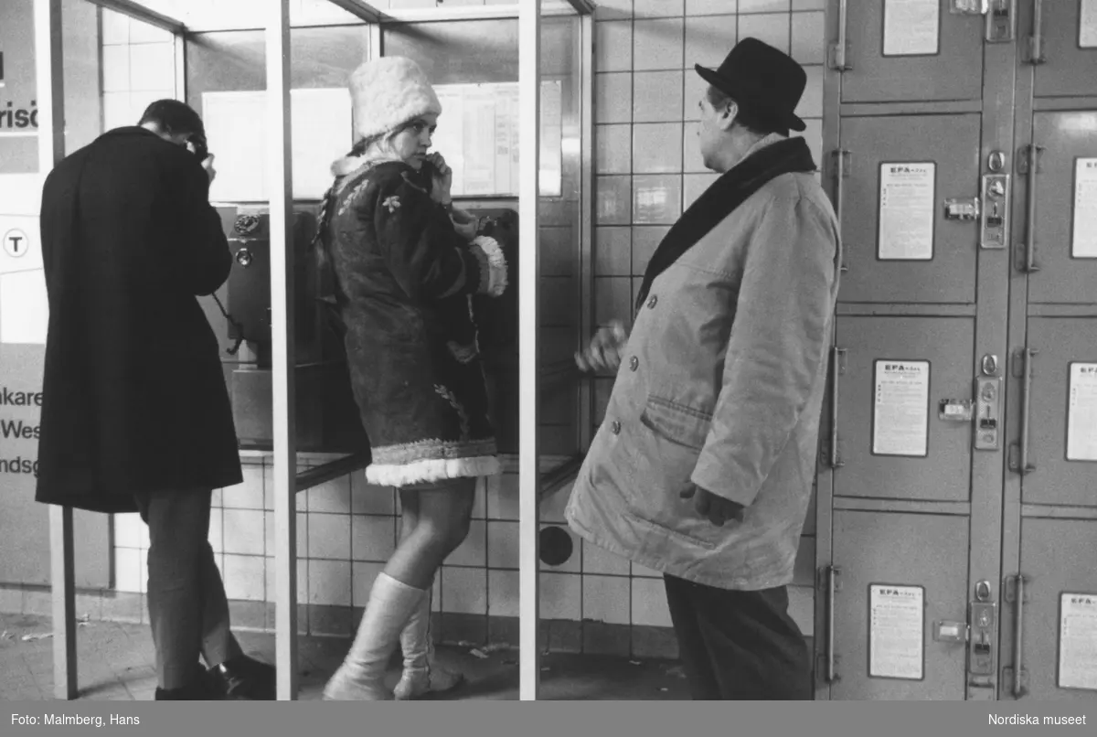 Stockholm 1968. 
Ung kvinna i telefonkiosk, köande man.