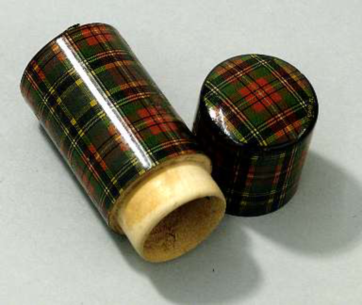 Fodral av trä, cylinderformat med skotskrutig dekor. På lockets översida står "Mc Beth" i guld. Bottenplatta av svart papper.