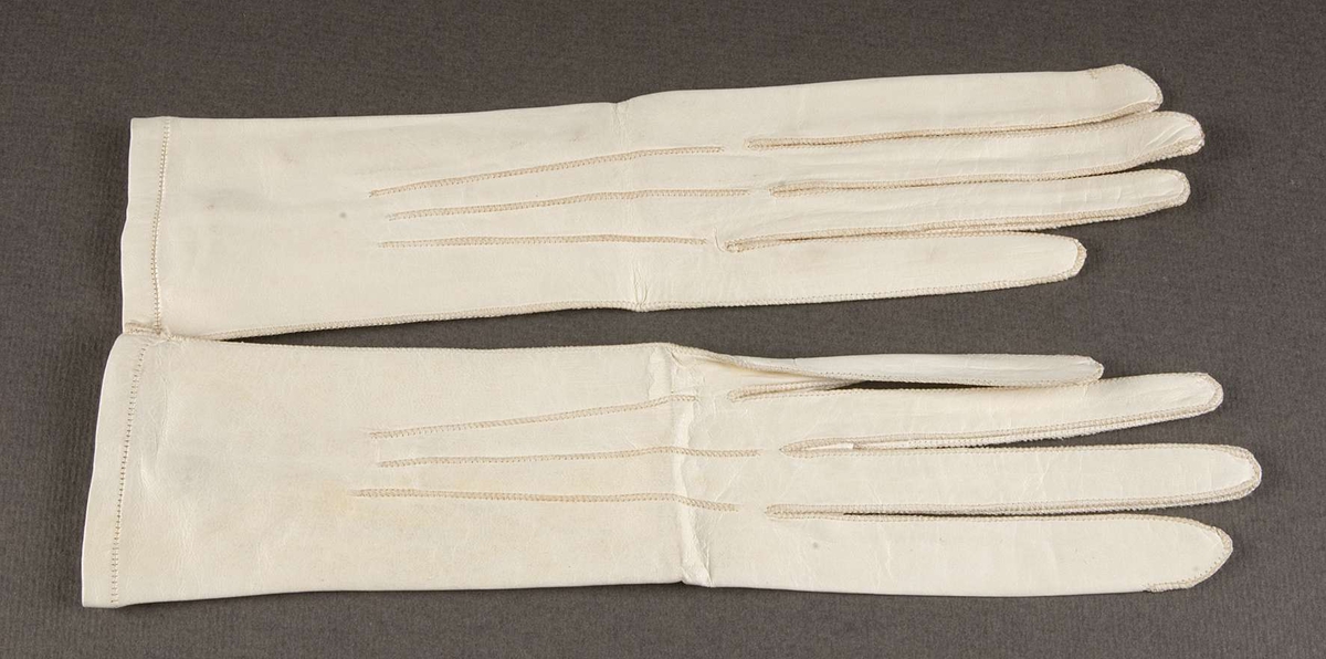 Två par vita glacéhandskar. Sprund vid handleden knäppt med knapp och knapphål Stämpel inuti en av handskarna: 10.6 3/4.
