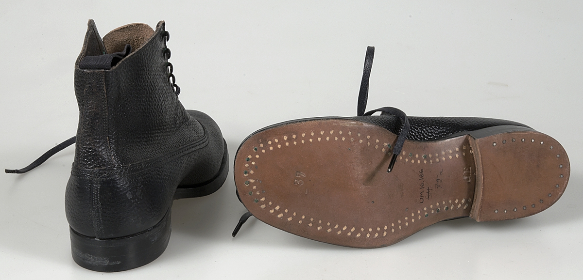 Ett par kängor av svart läder. Svarta vaxade skosnören. Ögla i hålen. Brun lädersula.