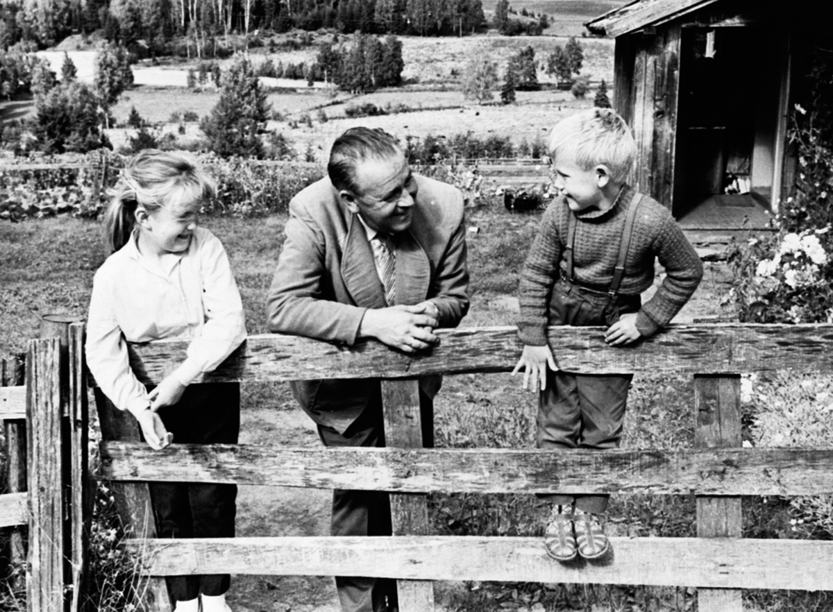 Alf Prøysen med 2 barn ved grinda foran Prøysenstua, Ringsaker. Barna er Mary Kristine og Jan Olaf Hagen. 1961.