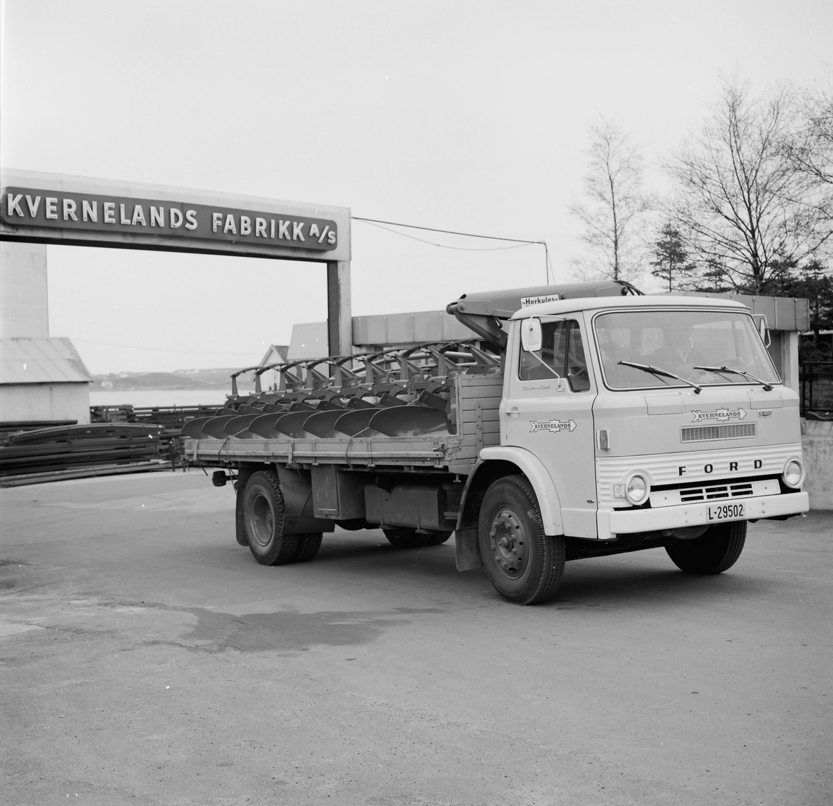 Kvernelands Fabrikk sin lastebil, merke Ford D-serie, kjører ut av fabrikkporten
(Ambolten 2.kv. 1969. Hr.Grude med fagprøve. 8-skjærs plog i krana Hall I og på lastebil)
