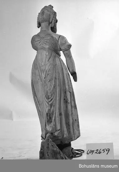 Föremålet visas i basutställningen Uddevalla genom tiderna, Bohusläns museum, Uddevalla.

Galjonsfigur från 1800-talets början. Kvinnofigur i empirklänning. Snäckor pryder håret som är arrangerat i en konstfull uppsättning med korkskruvslockar.
Vitmålad figur. Höger arm liksom vänster hand saknas.
Förgyllning i klänningens nederkant.
Svartmålad volutslinga som placerats som fundament.
Figuren bär spår av en tidigare ljusgrå målning.
Sockeln har spår av förgyllning.
Lagningar, en infälld bit vid mellangärdet och en på främre benet.
Stora torrsprickor.
Den högra armen saknas samt den vänstra handen.
Förvärvsomständigheter okända.

Ur handskrivna katalogen 1957-1958:
Galionsbild fr. o. 1800.
H. c:a 1,22 m. Br. c:a 0,38 m. Kvinnofigur i veckrik klädnad, stående på en rocailleliknande bas. Trä, vitmålat. H. armen borta, v. (Hand saknas) lagad. Sprickor o små hål. Bilden lagad på ett flertal ställen. Färgen avflagad.

Lappkatalog: 46

Litteratur: Hallén, Tore, Rüster, Reijo, "Galjonsbilder", Rabén & Sjögren, 1975. Vissa sidor finns kopierade, se Bilagepärm UM2659.
Kristiansson, Sten: Uddevalla stads historia II. 1953, s. 503.
Bilagepärm: "Vill du köpa en fågelskrämma? Would you like to buy a scarecrow?" Historien om galjonsfiguren Jenny Lind - The story about the figurehead of Jenny Lind. Skrift som troligen är författad av Karl-Eric Svärdskog, Göteborg år 1997 i samband med Tall Ships' Race i Göteborg  i augusti samma år. 16 s.