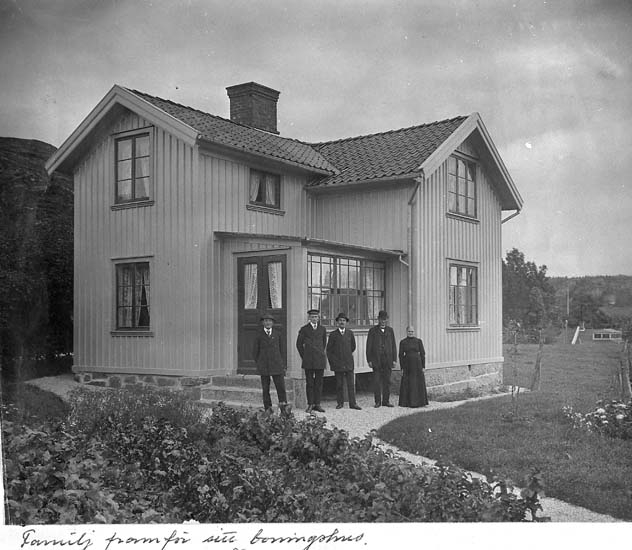 Text på kortet: "Familj framför sitt boningshus".


