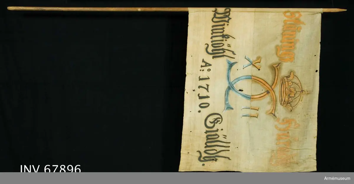 Duk:
Tillverkad av enkel vit linnelärft, sydd av två horisontella våder.

Dekor:
Målad endast från dukens insida. I mitten Karl XII:s namnchiffer, dubbelt C med X-II på ömse sidor, krönt med sluten krona i rött i det övre fältet, blått i det nedre. Text på ömse sidor om chiffret; upptill i gult med konturer i brunt och nedtill i svart.

Märkt:
På stången påskrift av bläck(?). Rest av ett lacksigill.