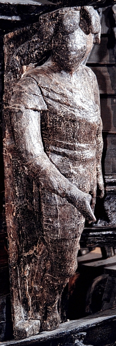 Skulptur av riddare i 1600-talsrustning med slutet visir.

Riddarens fältbindel är draperad från höger axel snett över bröstet och hjälmens plymer sträcker sig även ned utmed ryggen. Huvudet är kraftigt vridet mot höger och höger arm hålls framsträckt. Vänster arm förefaller ha varit sträckt utmed sidan. Vänster underben är delvis fragmentariskt men har tydligen varit placerat bakom höger ben som är lätt böjt.



Skulpturen är snidad i ett stycke så när som på armar, höftparti och fötternas ytterändar som är utförda separat och fastsatta med dymlingar och spikar. Troligtvis har skulpturen varit utrustad med svärd eller lans, kanske också sköld.



Skulpturen har ett mycket kraftigt bakstycke. Sett från sidan är bakstycket närmast kilformigt och dess baksida är upptill försedd med en klossliknande, snedställd "puckel" som i det närmaste täcker hela övre delen av bakstyckets baksida. I övrigt är denna slät. Bakstycket är snidat separat och skarven går utmed figurens rygg. Hjälmens plymer fortsätter ut över bakstyckets sidor. Genom bakstyckets kraftiga bredd upptill blir det parti som täcker figurens hjässa ovanligt långt. Figuren är i det närmaste diagonalställd i förhållande till bakstyckets bakre kant vilket ger den en framåtlutande hållning.



Text in English: Sculpture of a knight in seventeenth-century armour with closed visor.

His field badge is draped from his right shoulder across and over his chest. His elegant plumes fall down his back. The head is twisted sharply to the right and the right arm is held out in front. The left arm appears to fall beside his left leg beneath the field badge. The lower left leg is rather fragmentary but was obviously placed partially behind the right leg, which is slightly bent.



The sculpture has a very robust reverse side which, when seen in profile, is almost wedge-shaped. The upper reverse side has a block-like, angled "hump" which virtually covers the upper part of the back-planking's reverse side. Otherwise it is smooth. The whole of the back-planking has been carved separately from the actual figure, the seam runs along the back-planking's sides. Because the back-planking is so wide at the top there is a section that goes quite a long way out over the figure's head. The figure is positioned almost diagonally in relation to the reverse side of the back-planking, which gives the figure a forward-leaning posture.
