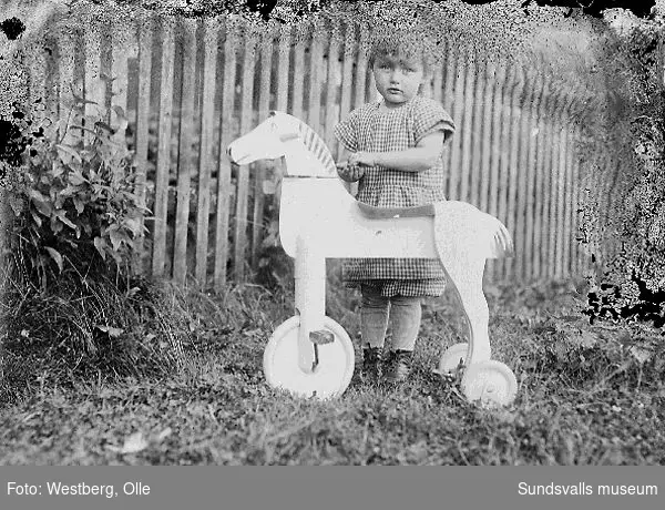 Anne-Marie Westberg, dotter till Linnea och Olle Westberg, med hjulförsedd leksakshäst i trädgården.