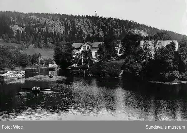 Selångersån från Widesbron. Vedpråm och roddbåtar. Sundsvalls barnhem på Åkroken skymtar fram bland träden.