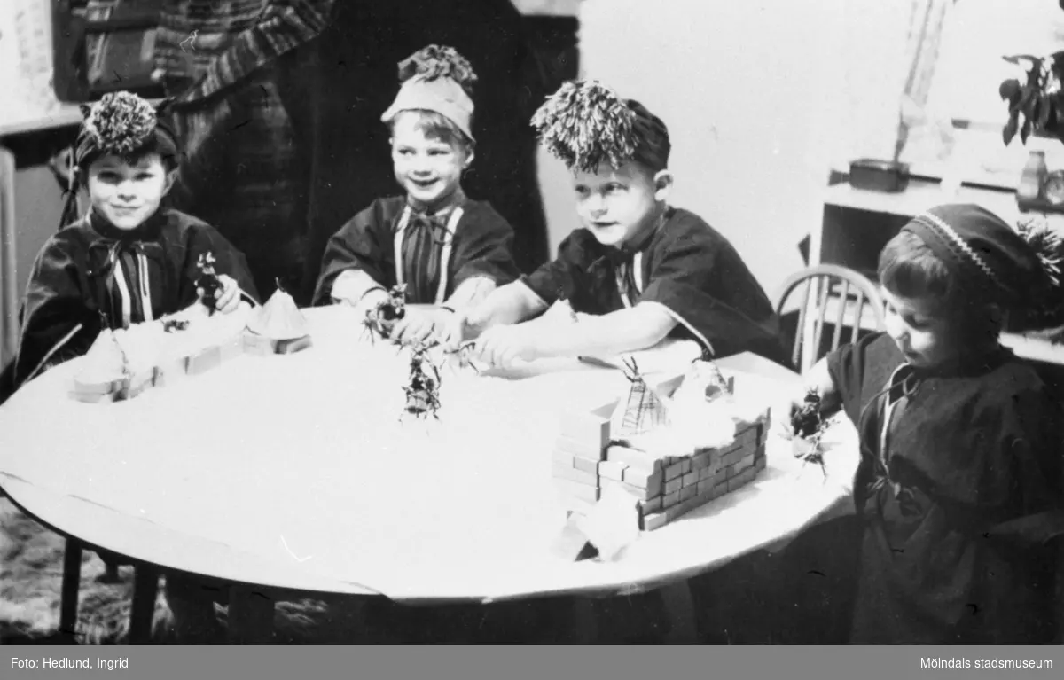 Bosgårdens barnträdgård 1938-1945. Barn som sitter vid ett bord utklädda till samer. Barnen har tillverkat sina egna enkla samekläder och mössor, med bl.a pärlträdning i lappfärger osv. Deras förskollärare Ingrid Hedlund hade gjort sitt examensarbete om samehantverk och denna kunskap använde hon i sitt pedagogiska arbete under flera år.