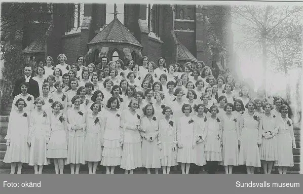 Kvinnliga konfirmander med präst utanför Gustav Adolfs-kyrkans kor, troligen 1930. Trea fr.v. i fjärde raden nerifrån är Maj-Britt Nyström (f. 1916), mor till Ingrid Hellqvist.