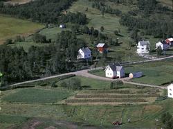 Flyfoto av gammelskolen i Fauskevåg. Hesjer og rød traktor i