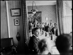 Gruppe kvinner og menn i stueinteriør, festdekket bord, vegg