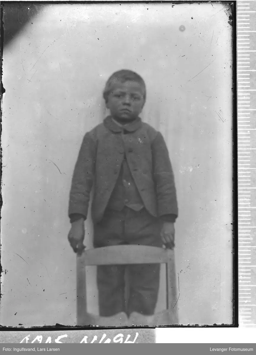 Portrett av en gutt ved en stol.