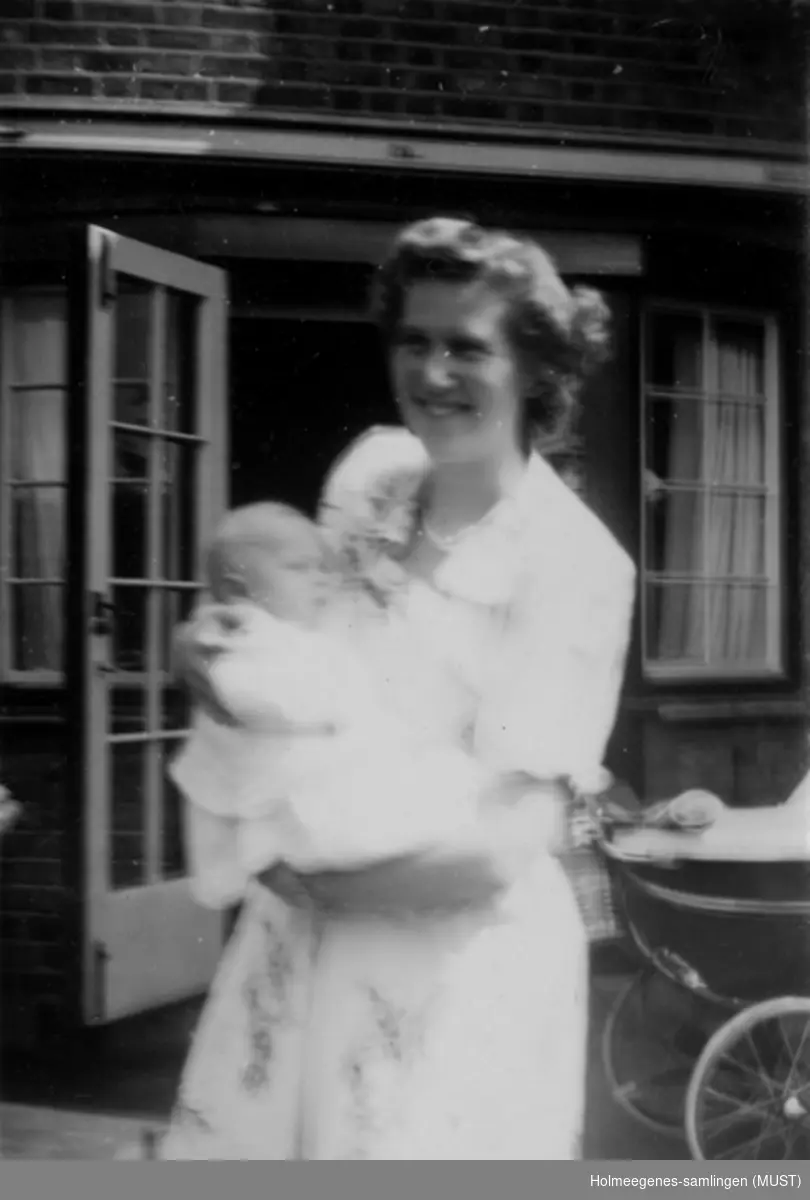 Kvinne med spedbarn foran et bolighus. Navn ukjent.