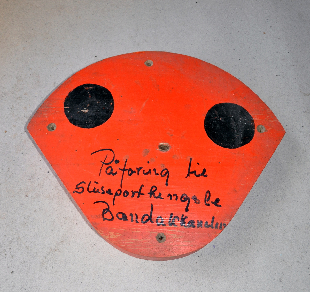 Støpemodell av tre med skruehull. Skive til å bygge opp porthengslene med. Oransj farge og to sorte prikker på.