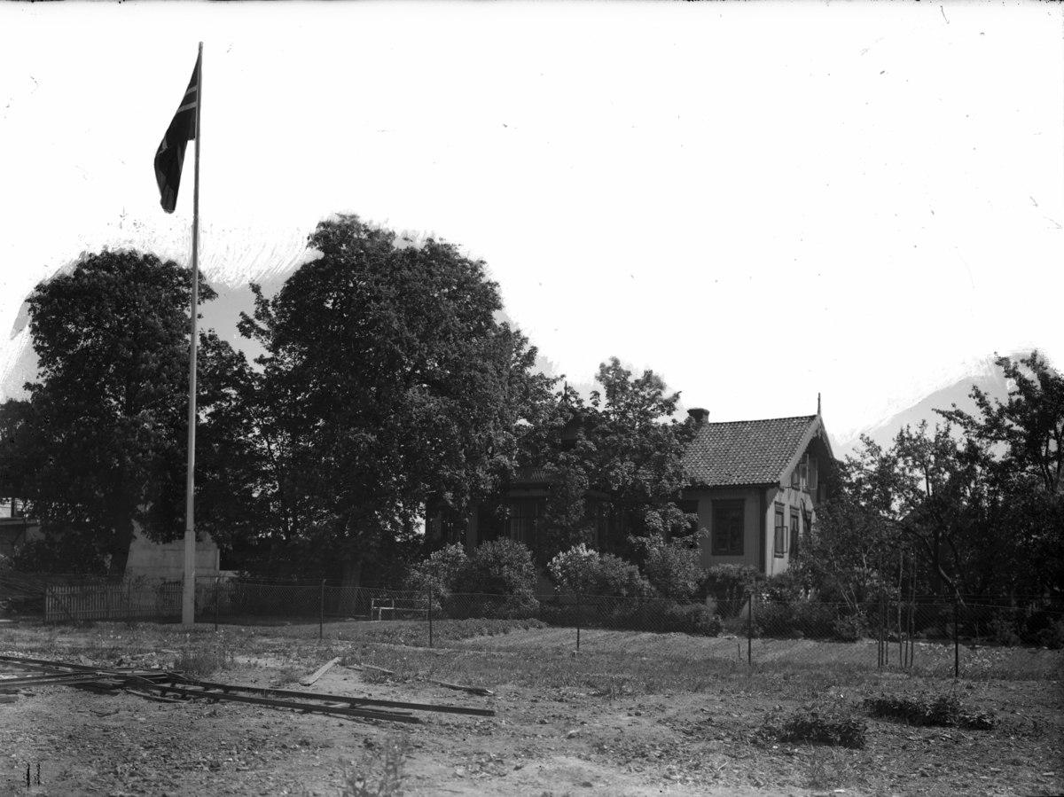 Flaggstang med hus i bakgrunnen fotografert