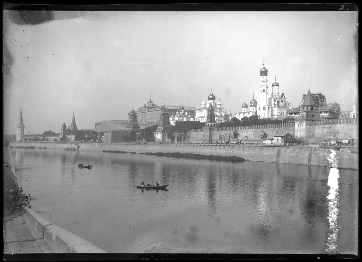 'Stadsvy, vy över flod med båtar, ekor. På andra sidan väg längs floden, med häst och vagnar, droskor, ekipage körande längs vägen som kantas av en hög mur. På andra sidan ett antal byggnader med torn och katedraler. Det är Kreml med kremlmuren med torn som ligger på andra sidan Moskvafloden. ::  :: Ingår i serie med fotonr. 5286:1-18. Se även fotonr. 5269-5292 med bilder från Stuxbergs resa till Kaukasien.'