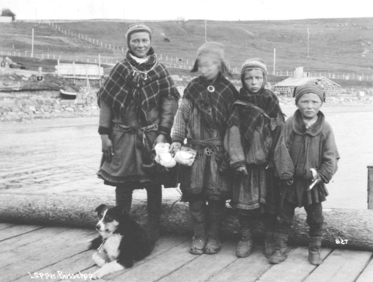 Samisk familie, en ung kvinne og tre barn, fotografert på kaia i Bossekop
