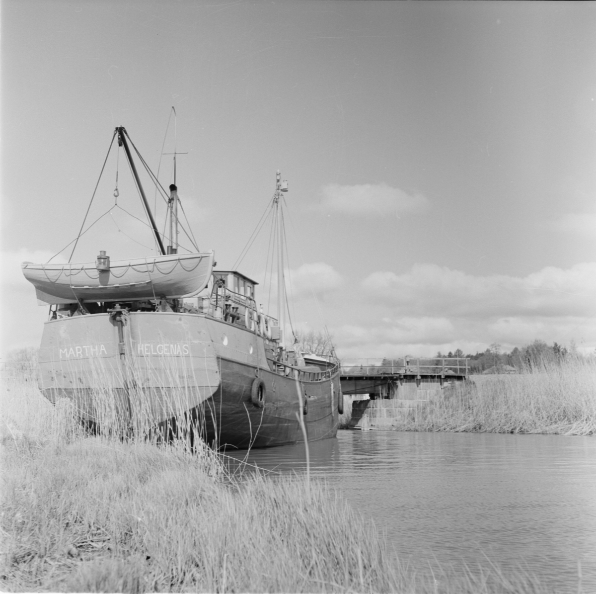 Lastbåten "Martha" ligger i vattnet vid Örsundsbro, järnvägsbron i bakgrunden, Uppland 1950-60-tal
