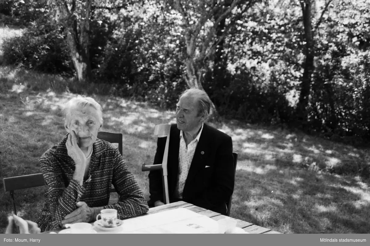 Lindome Hembygdsgille firar 20-årsjubileum på Börjesgården i Hällesåker den 23 juli år 1983. En kvinna och en man i trädgården.

För mer information om bilden se under tilläggsinformation.