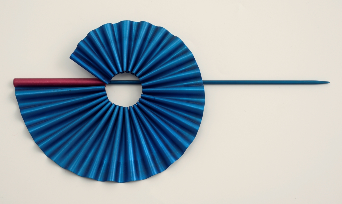 En foldet blå spiral festet til en blå nål med en lilla hylse. Alle komponentene er laget av eloksert aluminium.