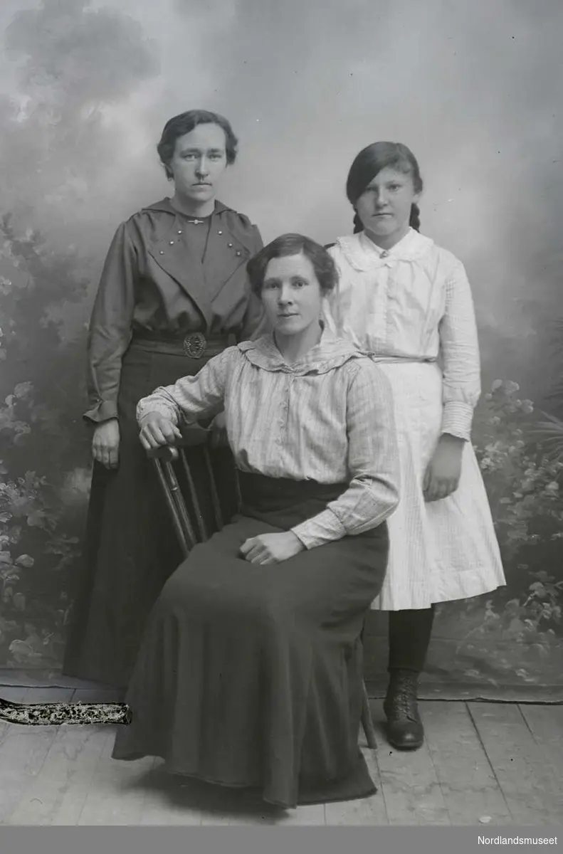 Portrett. Tre kvinner. En sitter på en stol, to står bak.