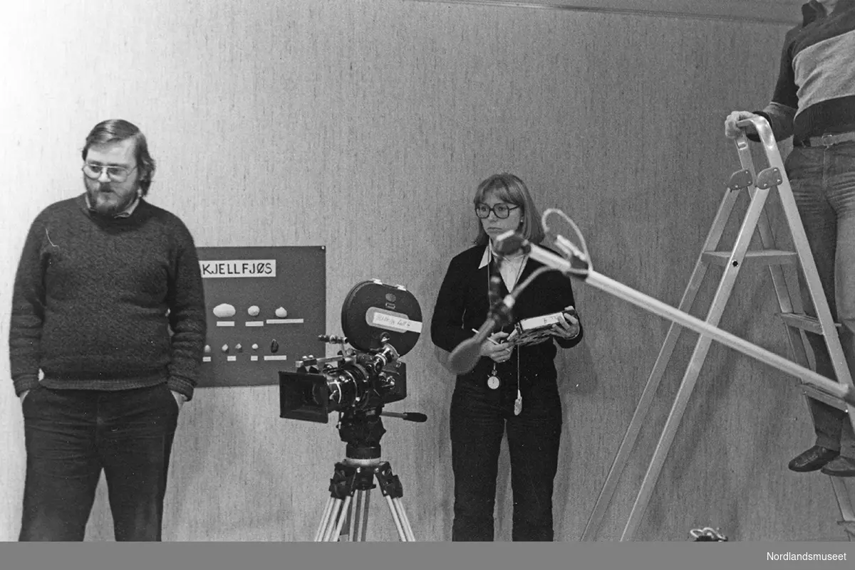 lekeuke på Nordlandsmuseet, TV`s "Halvsju" tar opptak av leking med skjellfjøs på Nordlandsmuseet filmkamera, tre voksne, gardintrapp og plansje på veggen.