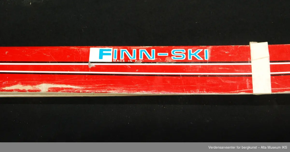 Røde laminerte ski, laget i Finland med norske bindinger. Stripete mønster.
