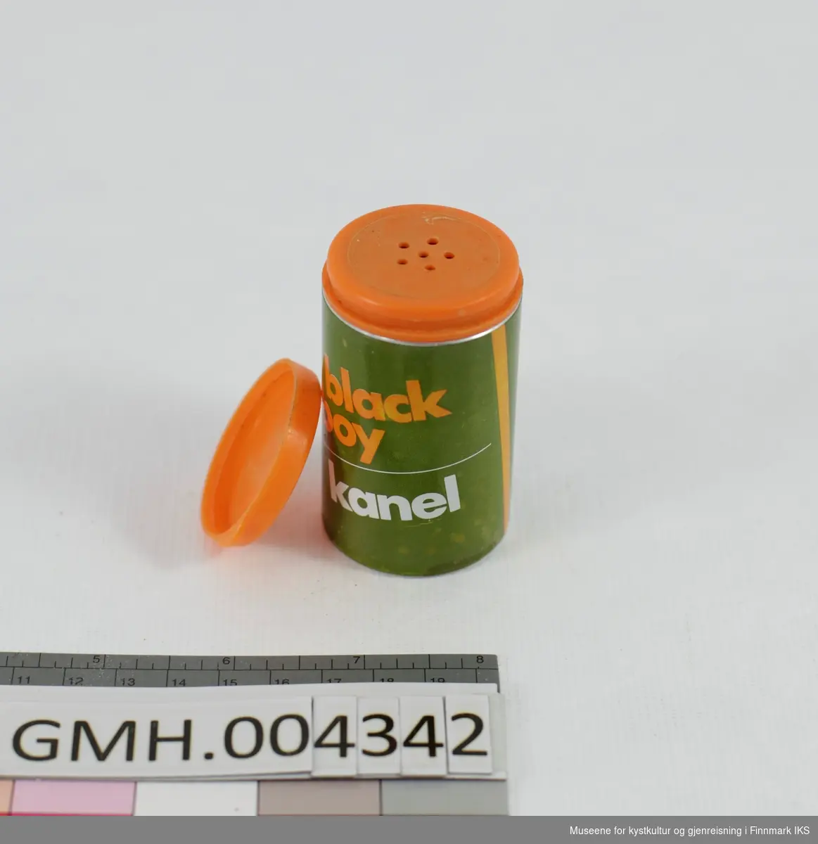 Den sylinderformede boksen er laget i metall og har en olivengrønn design med hvite og oransje bokstaver påtrykt. Lokket er av fleksibel, oransje plast og sitter på et fast lokk med strøhull i av samme material og farge. Emballasjen er tom.