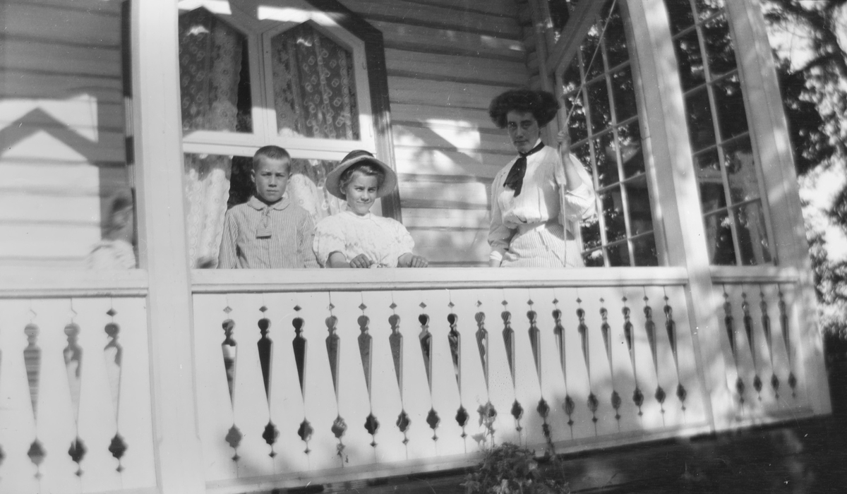 Celina Ihlen Mathiesen drar i en snor . Hun står sammen med Haaken Christian og Celina Marie og et barn trolig Ise (Louise), som bare synes så vidt, på en veranda.