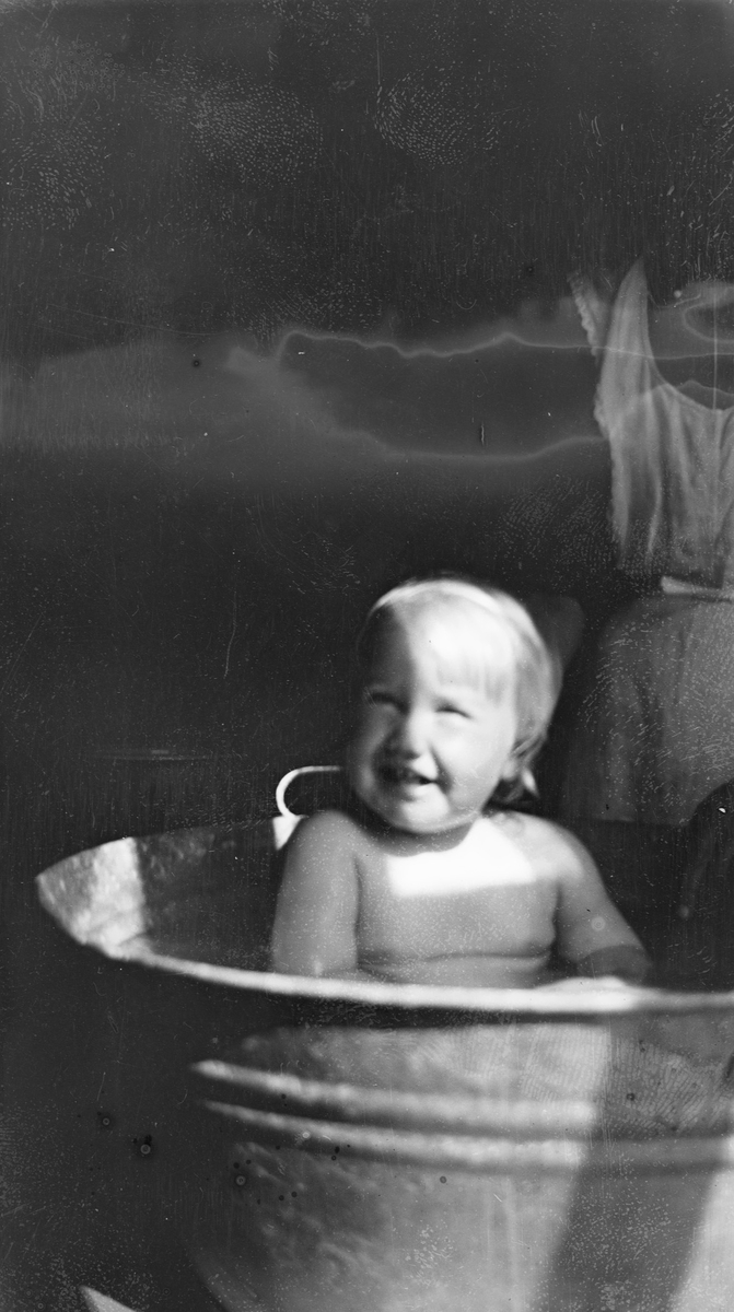 Iacob Ihlen Mathiesen bader i en sinkbalje. I bakgrunnen står en kvinne med forkle.