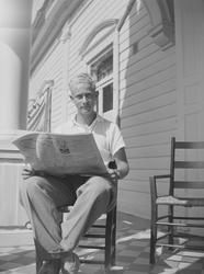 En ung mann sitter på en stol og leser en avis. Han sitter u