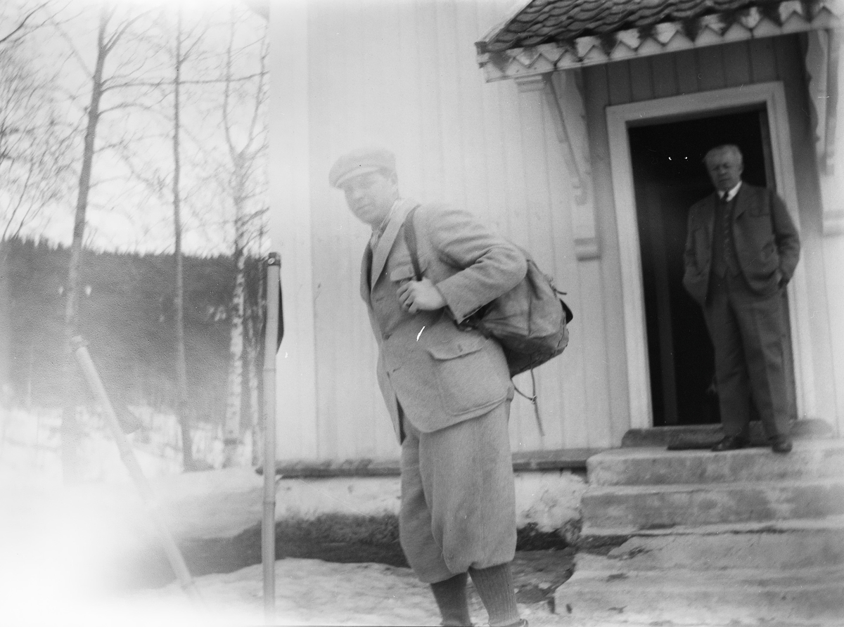 Christian Pierre Mathiesen står på trappen til et hus foran en åpen dør og ser mot fotografen. Carl med ryggsekk og kledd i sportsklær.