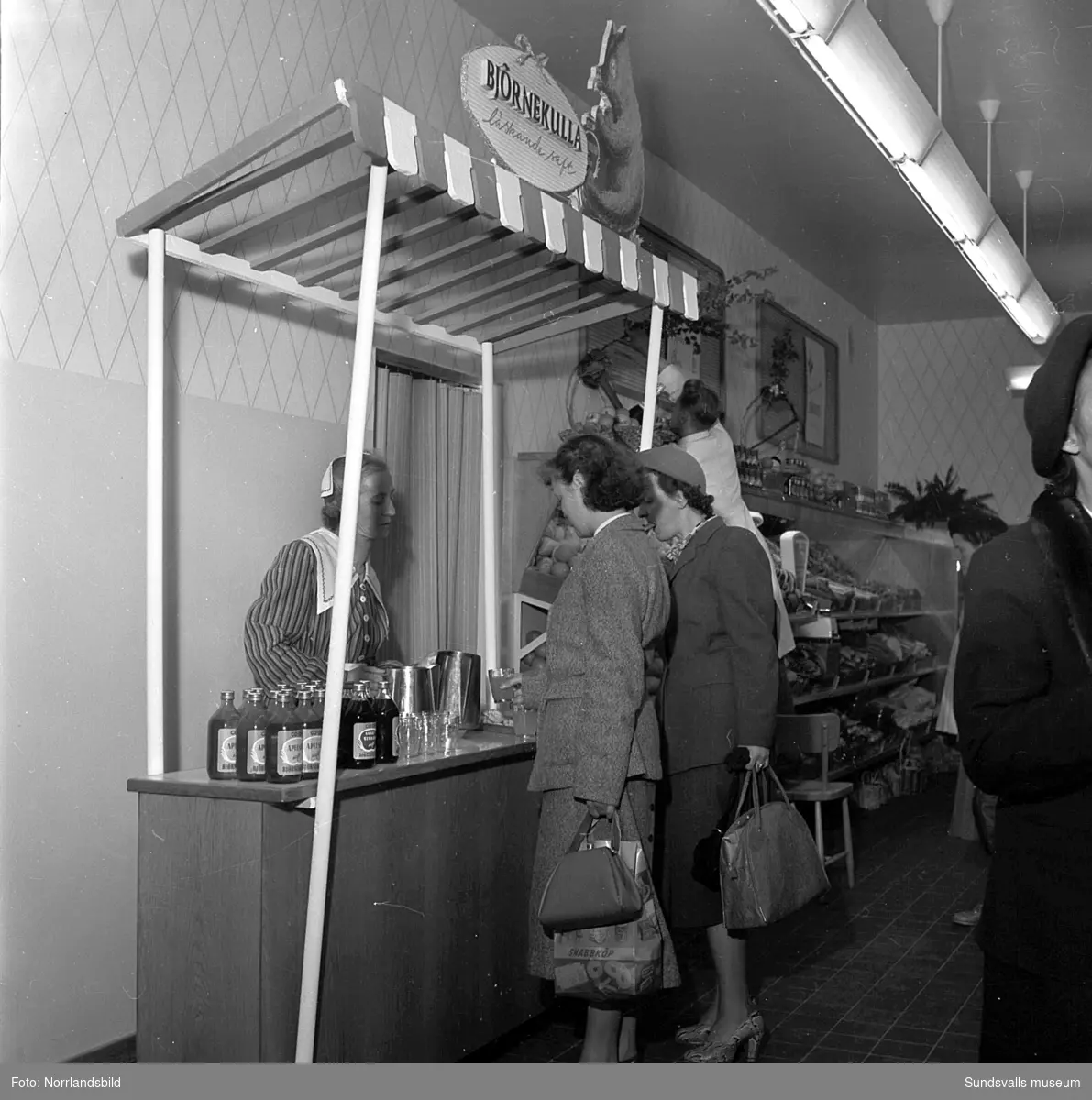 Konsums snabbköp vid Bankgatan har byggts ut 1952 och en kund är sångerskan Alice Babs som inspekterar fruktavdelningen och handlar för fem kronor och femtiosju öre.