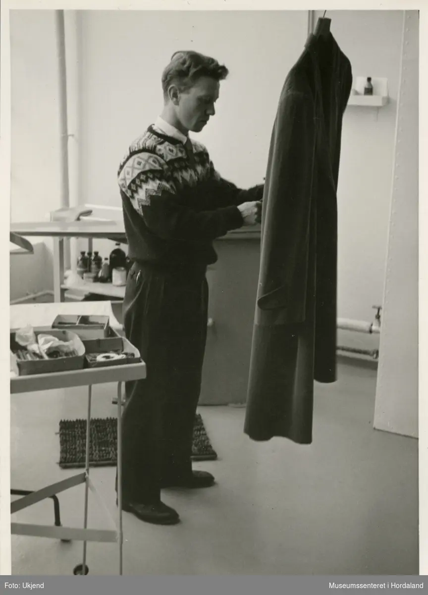 Mann arbeider utfører detasjering (flekkfjerning) på frakk ved Wilhelm Kahrs Kemisk Renseri & Farveri, Bergen.