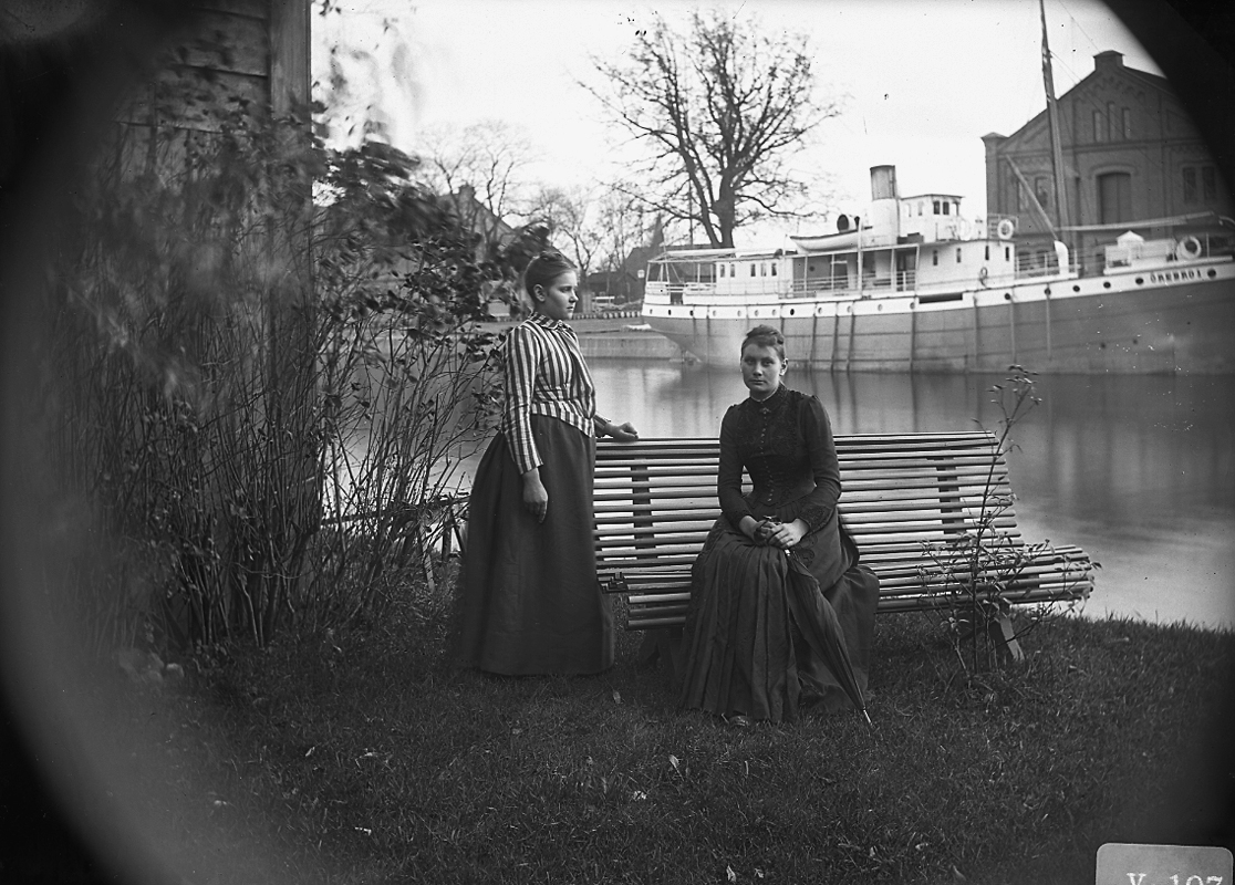 Två kvinnor.
Hamnmagasinet och en ångbåt i bakgrunden.
Bilden är tagen på 1880-talet. Båten "Örebro I" byggdes 1888.