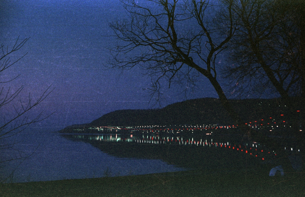 En nattbild tagen från stranden vid Vättersnäs utanför Huskvarna. E4:ans vägbelysning speglar sig i Vätterns vatten förbi Norrängen mot vista kulle.