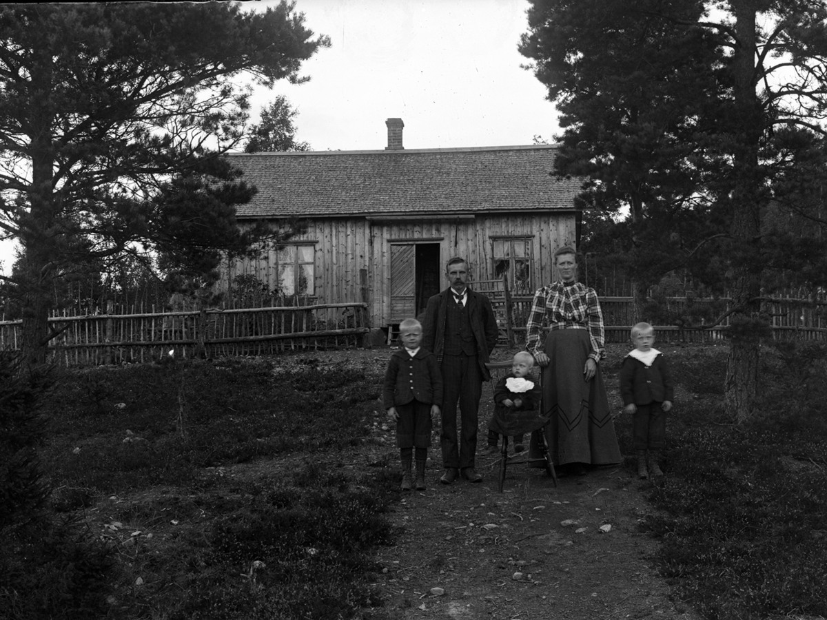 En familj fotograferad framför huset i Nyslätt "Skomakarns". Bilden är tagen på våren/sommaren 1911. Skomakare Johan Andreasson och makan Selma med tre barn: Karl (till vänster i bild) Gunnar och Klas som sitter på en barnstol. Selma är havande med Anna som föddes den 27 sept 1911.