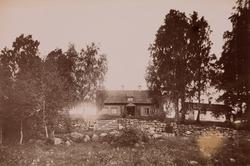 Et lite hus i midten av noen trær bak et steingjerde med por