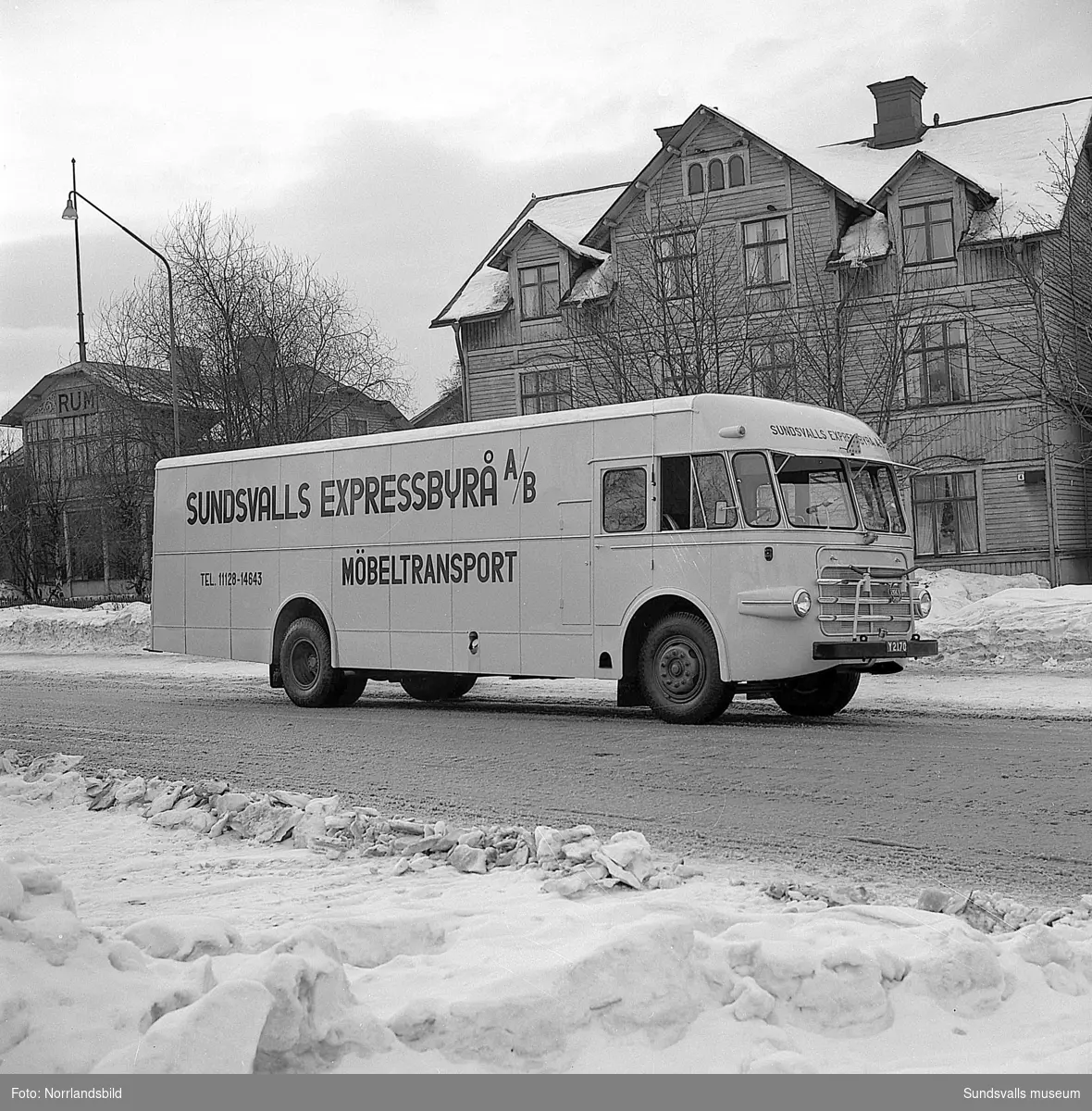 Sundsvalls Expressbyrå AB. Möbeltransportbuss fotograferad på Parkgatan. De båda träkåkarna i bakgrunden är numera rivna.