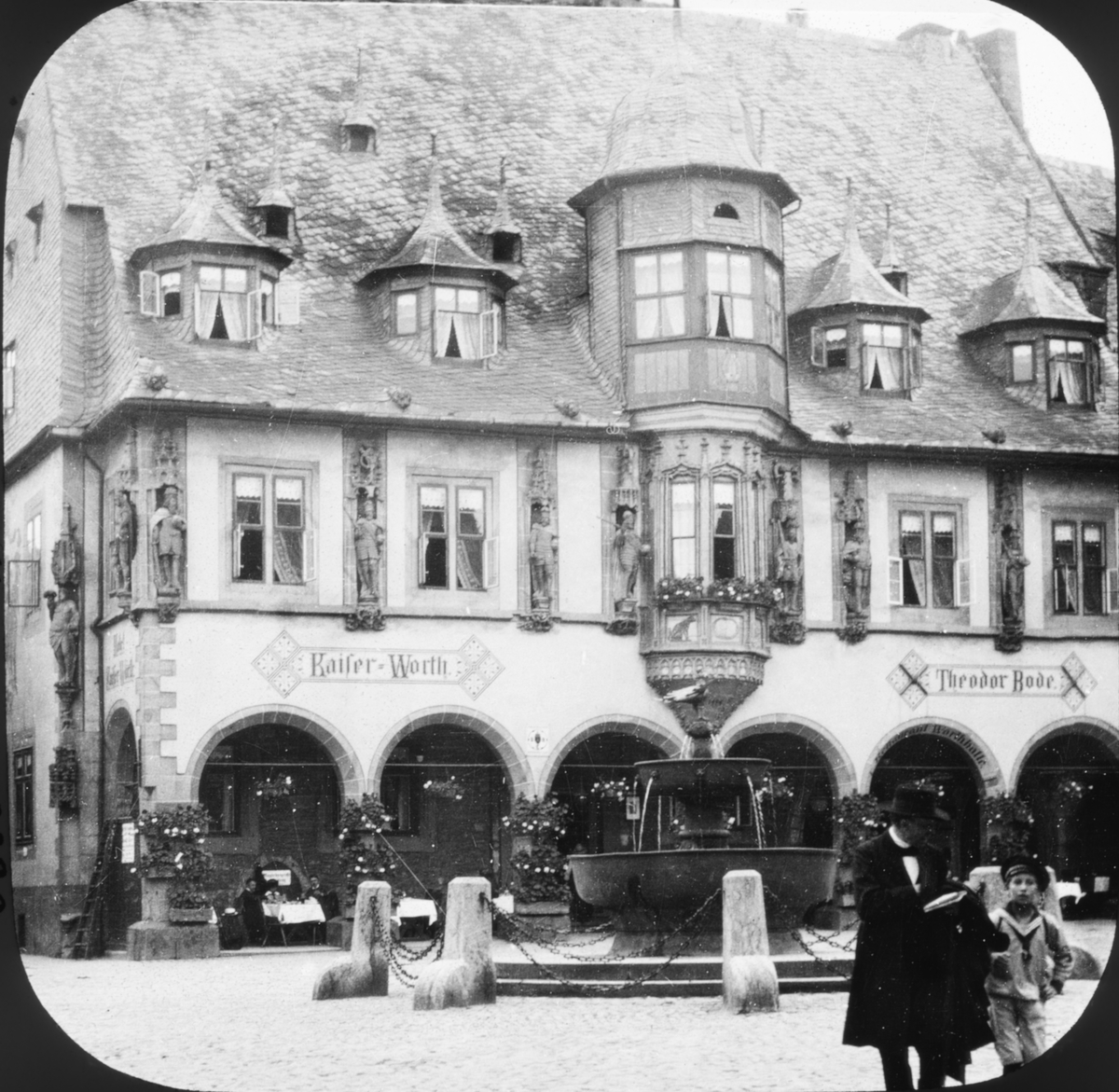 Skioptikonbild med motiv av Hotel Kaiserworth vid torget i Goslar.
Bilden har förvarats i kartong märkt: Resan 1907. Goslar 8. Text på bild: "Baggens plat".