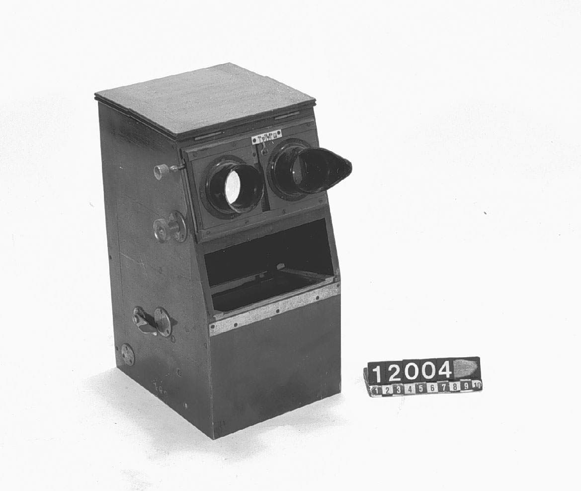 Stereoskop för bilder 5 x 10 cm, med inställning för ögonavstånd och automatisk bildväxling samt magasin för 80 st bilder. 
Nr instansat under toppluckorna: "752376". 
Ena ögonmusslan skadad. Bottendelen innehåller 4 stycken bildkassetter.