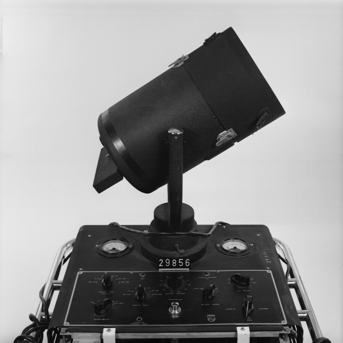 Stroboskop med blixtlampa tillverkad av krymplackerad svartplåt, beslag och handtag i förnicklad metall, monterad på fyra hjul varav två svängbara. Öppen baksida med plexiglas. Märke GM 5500/5501 Nr. 610. V 110-245 W 500. P/S 40-60.