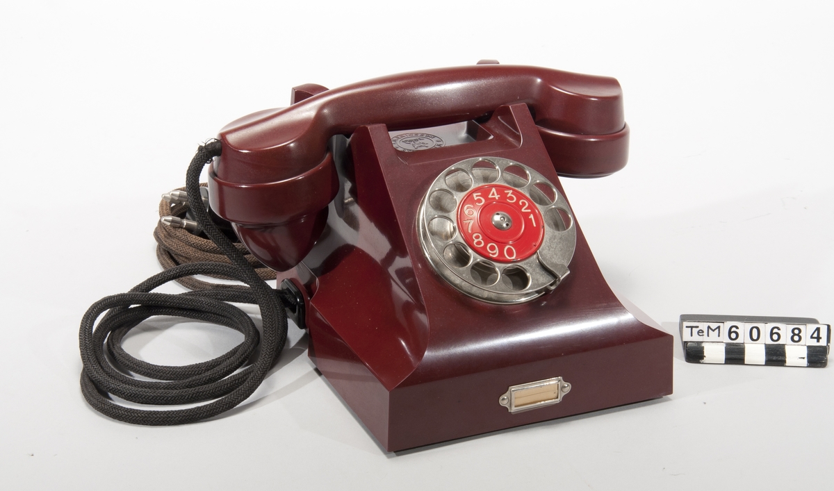 Telefonapparat, bordsmodell av röd bakelit. För AT-system.