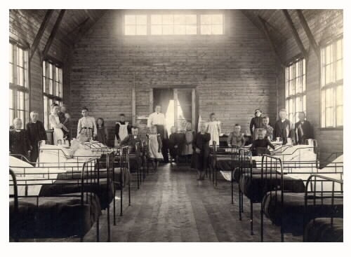 Interiör från Kustsanatoriet Apelviken år 1905. Sjuksal i den gamla träpaviljongen. En grupp patienter och personal står vid väggen. Solljuset var viktigt så byggnaden hade stora fönster, även i gaveln.