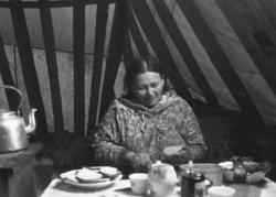 En kvinne sitter i lavvoen og smører brødskiver. Kåfjord 196